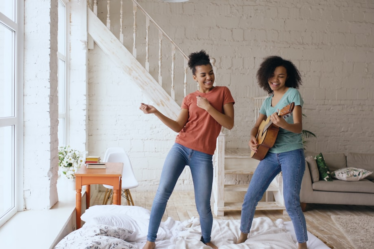 Two women dancing and playing guitar indoors. — Foto por Vitaly Gariev na Unsplash