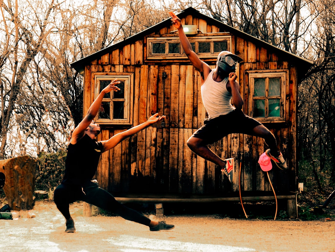 a couple of people playing frisbee in front of a log cabin — Foto por Jamal Selolwane na Unsplash