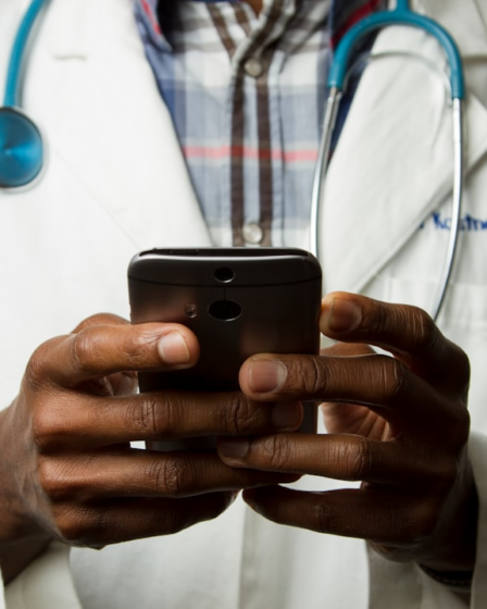 person wearing lavatory gown with green stethoscope on neck using phone while standing — Foto por National Cancer Institute na Unsplash