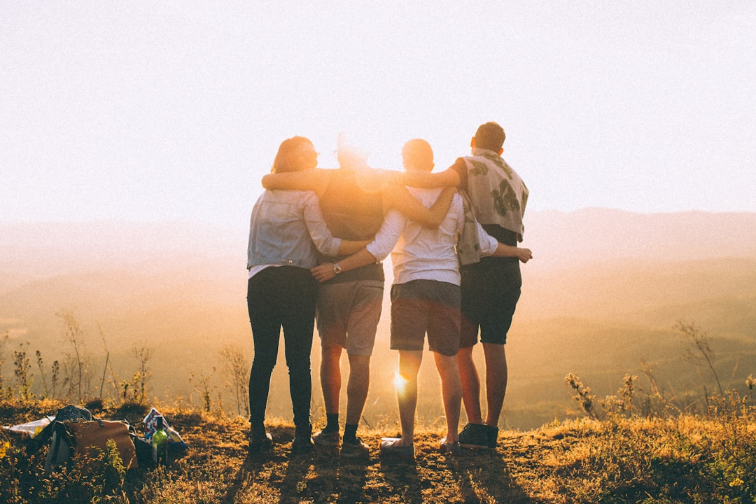 four person hands wrap around shoulders while looking at sunset — Foto por Helena Lopes na Unsplash
